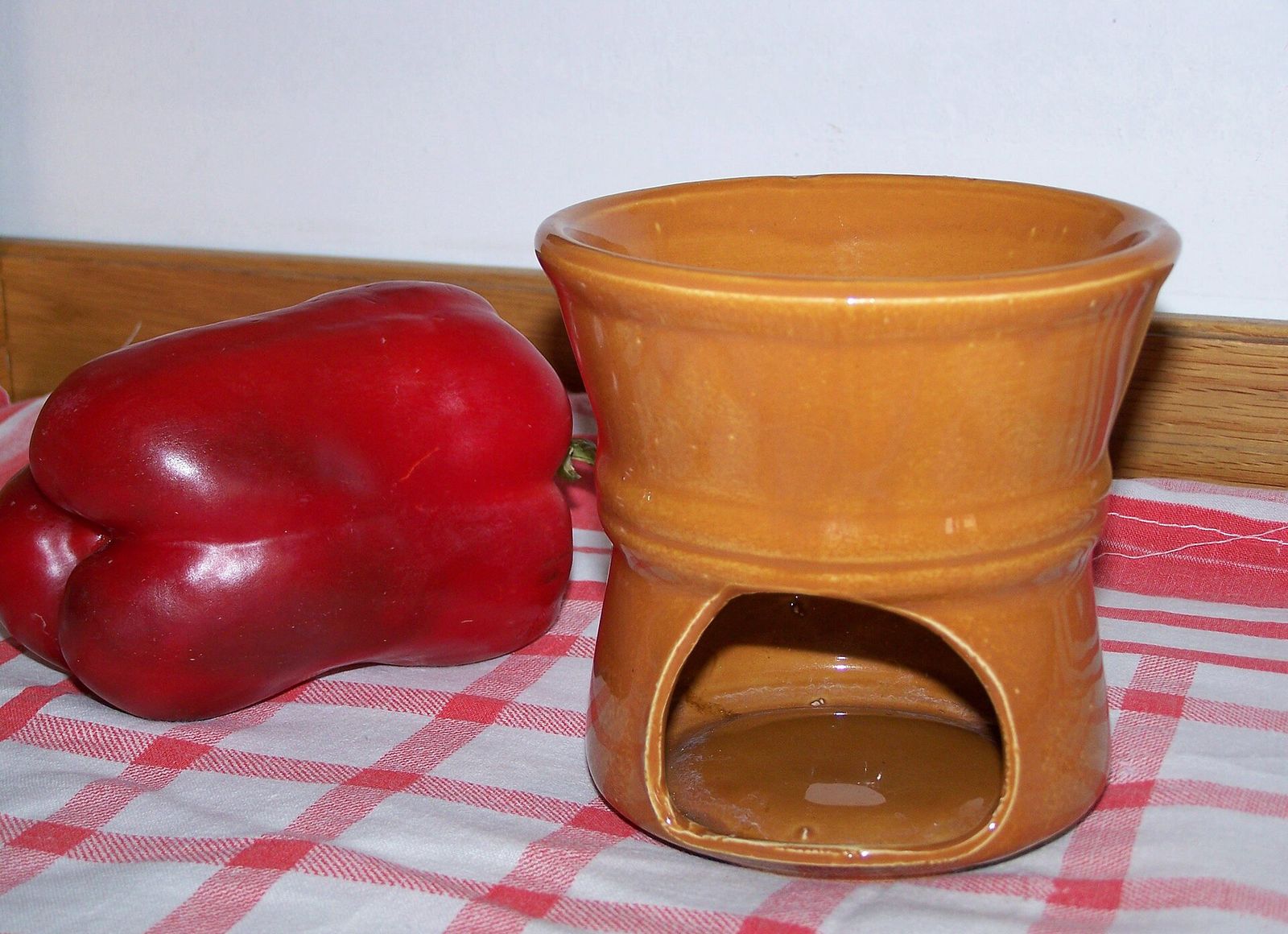 Un fujot in terracotta smaltata per la bagna cauda accanto a un peperone rosso, su una tovaglia a quadri bianchi e rossi