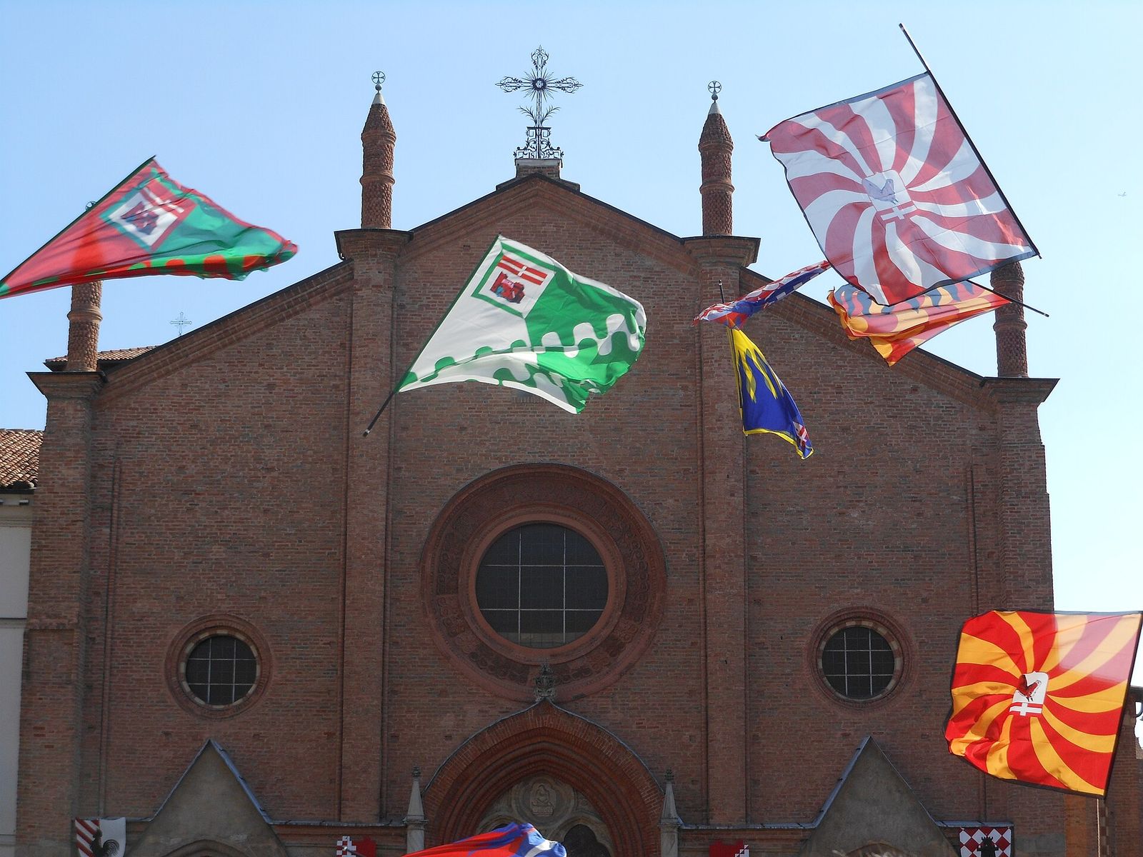 Bandiere colorate degli sbandieratori lanciate in aria davanti alla facciata in mattoni della Collegiata di San Secondo ad Asti