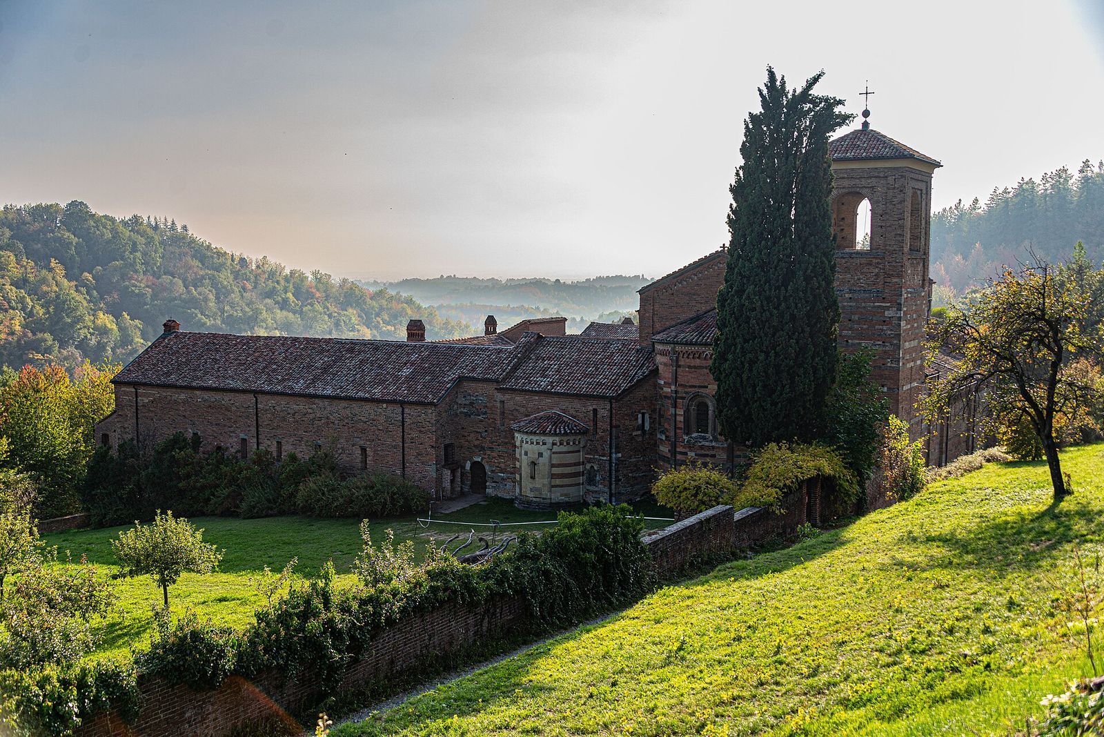 Il complesso dell'abbazia di Santa Maria di Vezzolano tra prati e boschi sulle colline di Albugnano, con il campanile e un alto cipresso